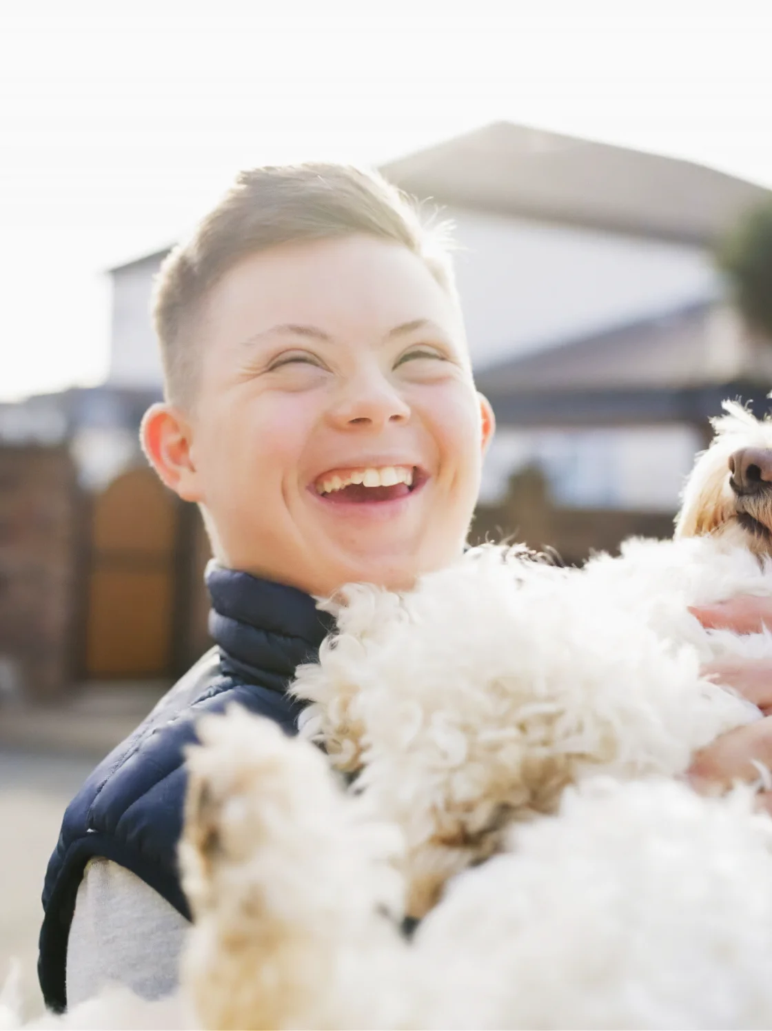 A boy holds a fluffy white dog, smiling happily as they enjoy a moment of joy and companionship together.