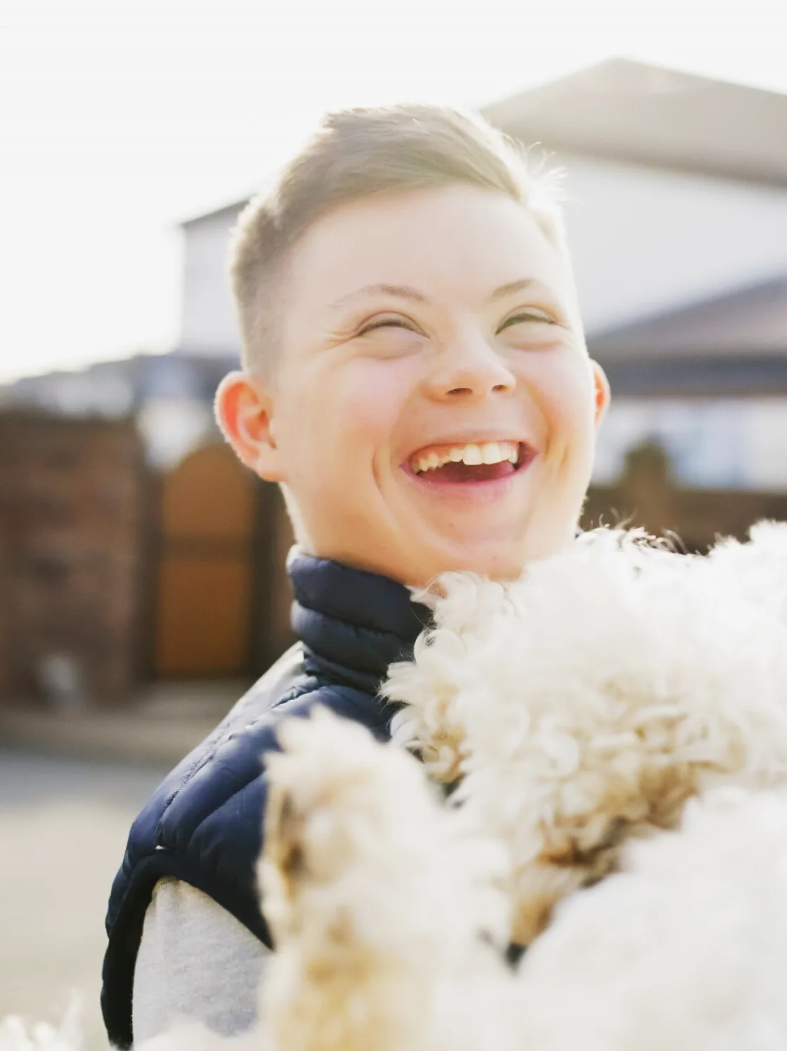 A boy holds a fluffy white dog, smiling happily as they enjoy a moment of joy and companionship together.